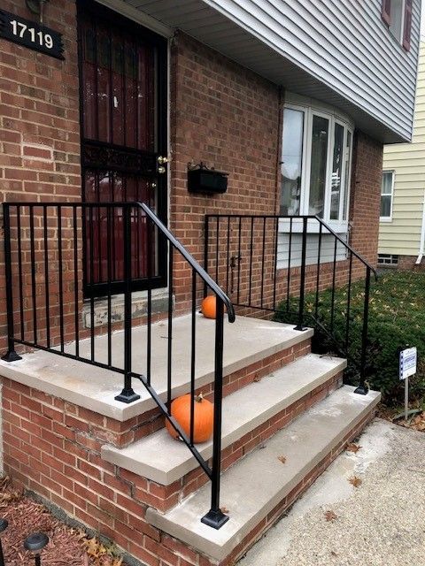 Brick rowhouse entry with black railings and orange pumpkins on the steps