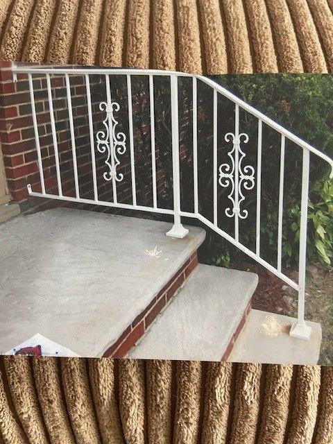 White metal railing with decorative scrollwork beside outdoor concrete steps and brick wall