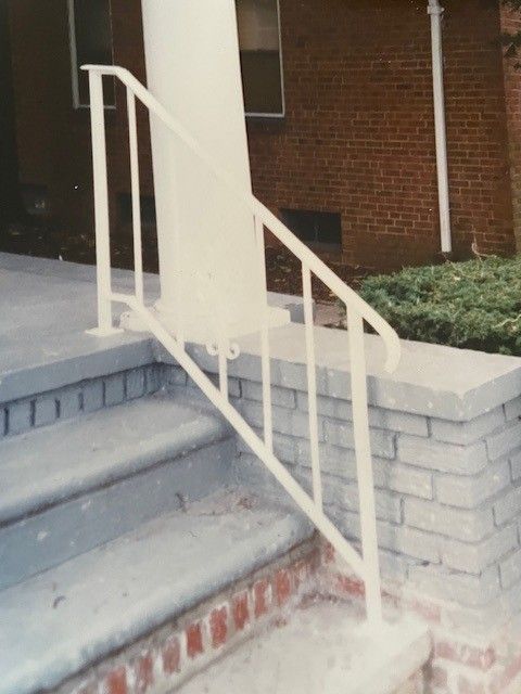 White metal handrail beside concrete steps leading to a brick building entrance