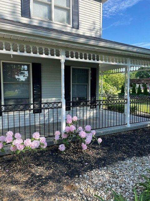 Front porch of a gray house with black railings and pink flowers in front.
