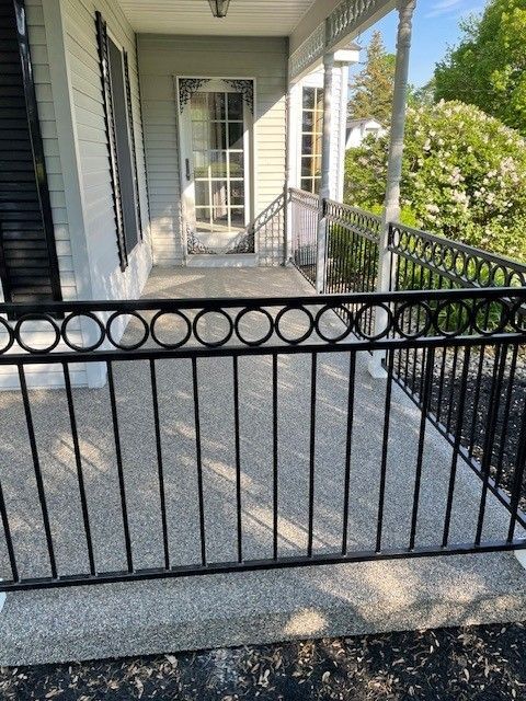 Front porch with black metal railing, concrete floor, white door, and screened windows in bright daylight
