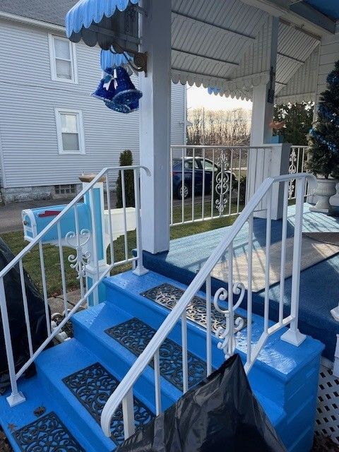 Blue-decorated front steps and porch with white railings, blue stairs, and a black trash bag in the foreground