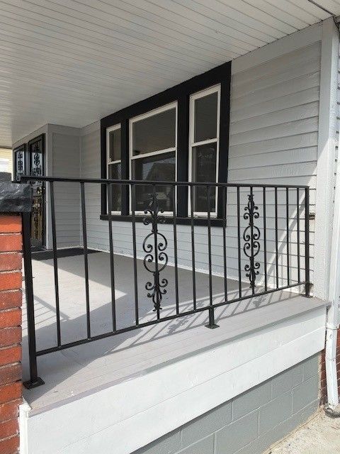 Covered front porch with black railing, white siding, and a gray concrete floor.