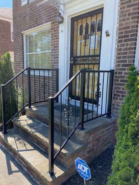 Front porch with black metal railings, steps, and a decorative front door on a brick townhouse.