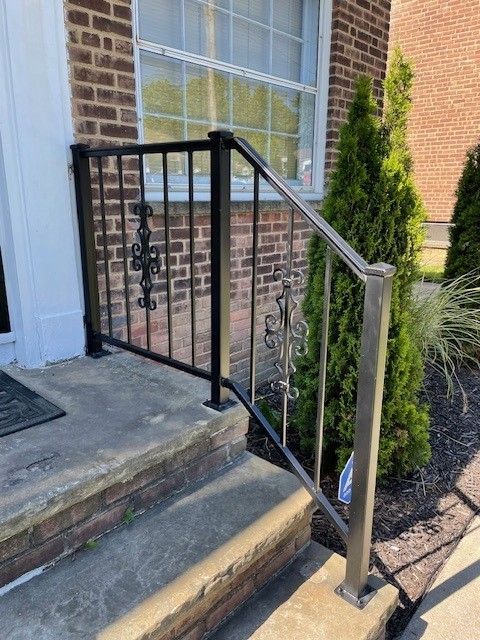 Front steps with a black metal handrail and silver post beside a brick house entrance