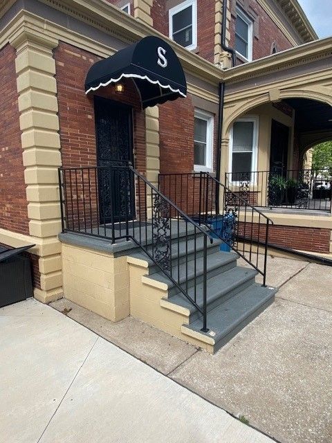 Front steps of a brick building with a black awning, metal handrails, and a small accessible ramp.
