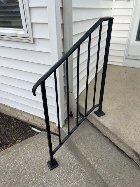 Black metal handrail along concrete steps beside a house exterior.