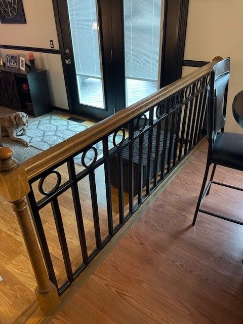 Interior balcony railing with black metal balusters beside a hardwood floor and glass doors