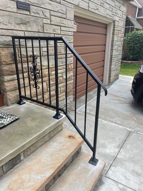 Stone front steps with black metal railing beside a garage and driveway