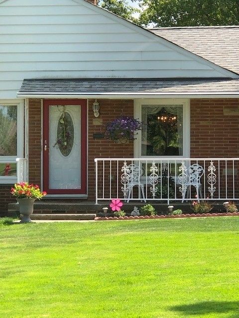 Front porch of a brick house with white railing, hanging flowers, and a bright green lawn