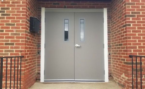 Closed gray double doors in a brick building entrance with narrow windows Closed gray double doors in a brick building entrance with narrow windows
