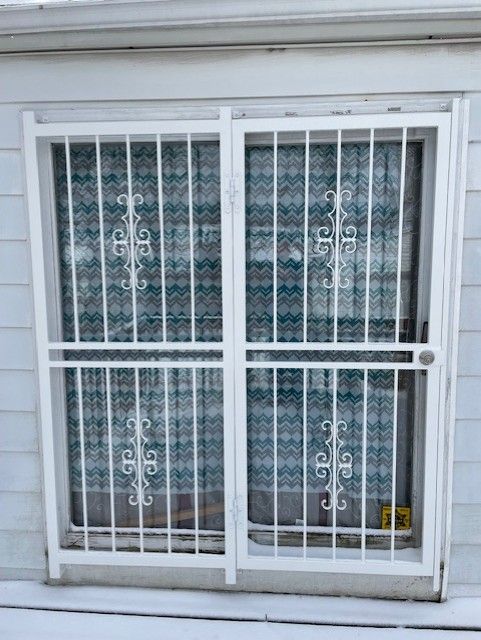 White metal security gate over a window with patterned curtains behind it