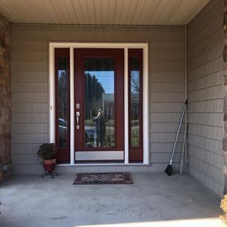 Covered front porch with a white-framed glass front door, potted plant, broom, and small rug.