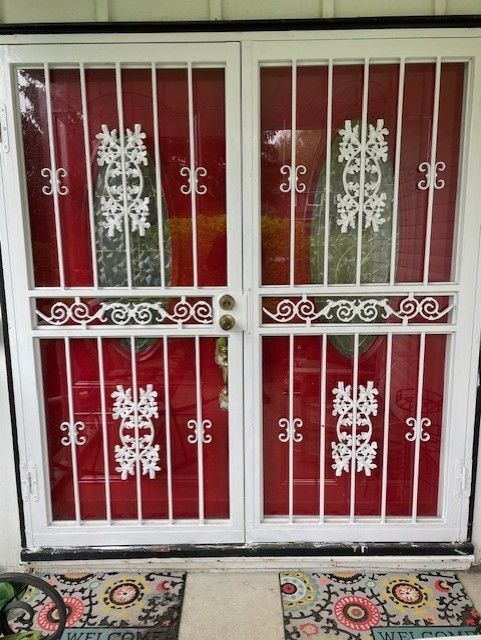White metal double security door with red panels and snowflake decorations, above patterned doormats.