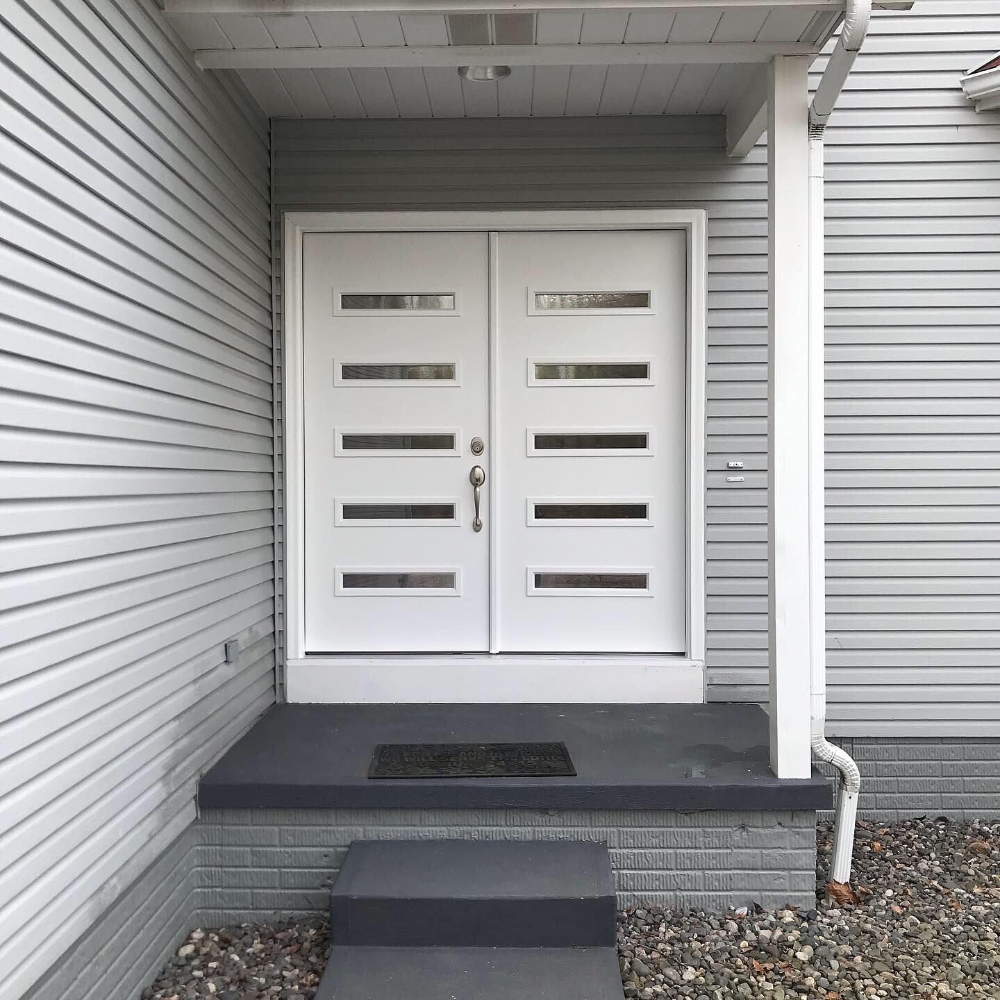 White double front doors with five horizontal glass panes each, set in a light grey home entry with a small concrete step.