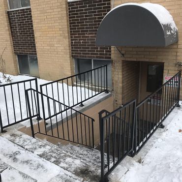 Snow-covered apartment entrance with black metal railings and a gray awning over stairs. Snow-covered apartment entrance with black metal railings and a gray awning over stairs.