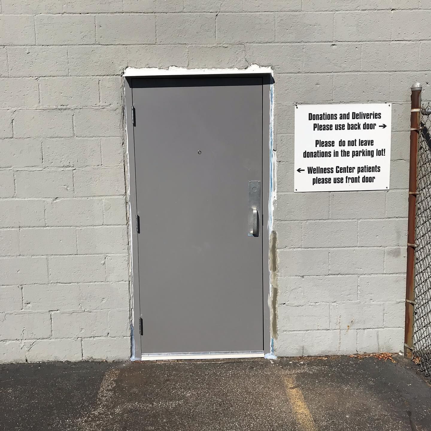 A grey metal door in a cinderblock wall with a sign directing deliveries to the back and patients to the front door.