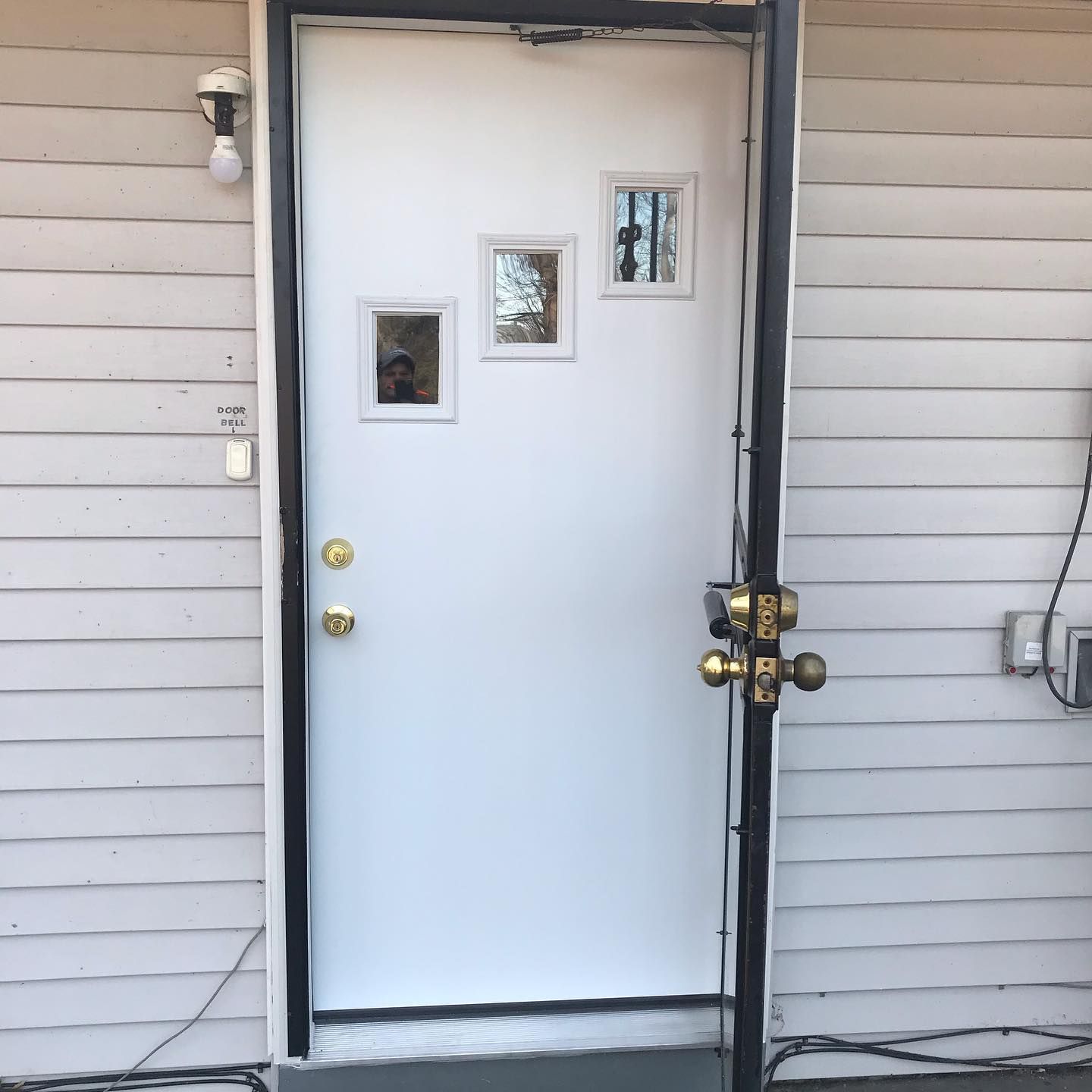 A white exterior door with three rectangular windows, set against light horizontal siding.