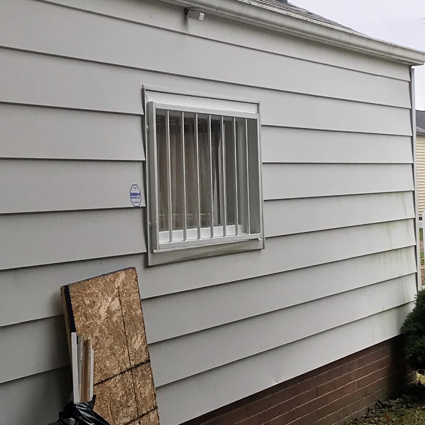 A side view of a light gray house featuring a window with a metal security grate and a small security system sticker.