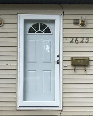 White front door with half-moon window on beige house siding, house number 2625, and a mailbox.