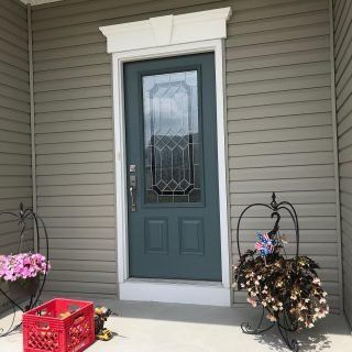 Front porch with a blue door, white trim, potted flowers, and a red crate.