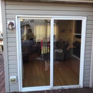 Sliding glass door on a gray-sided house, showing a living room inside.