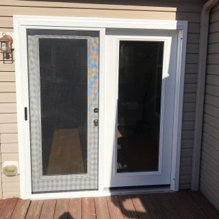White sliding screen door and dark glass patio door on a house exterior.