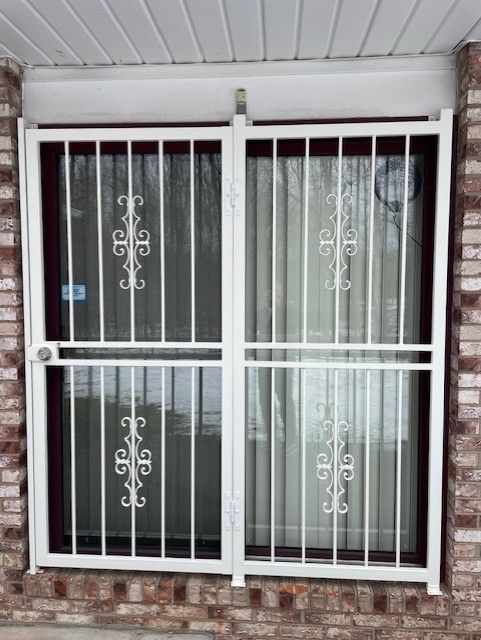 White security bars on a brick house window with curtains behind it