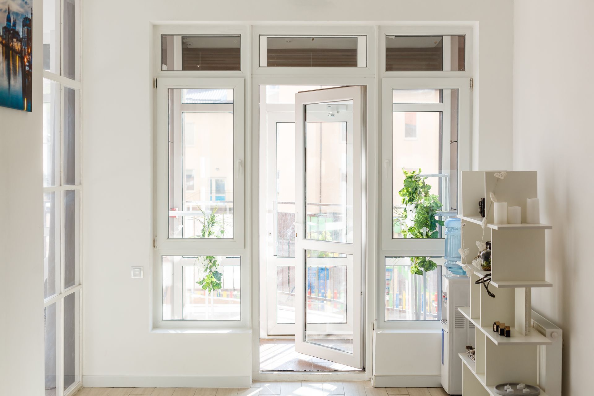 Bright white room with large windows, a glass door, and a small shelf with decor on the right