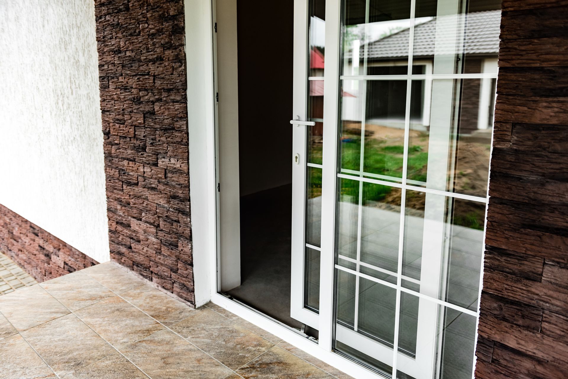 Sliding glass door entrance beside brick wall and white stucco, reflecting outdoor greenery and windows