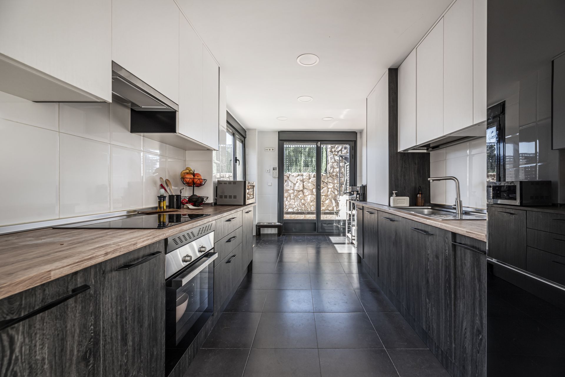 Modern kitchen with white cabinets, dark island, stainless appliances, and glass doors leading outside