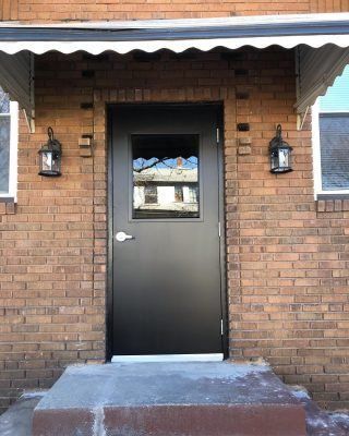 Black front door beneath a brick awning, flanked by two wall lanterns