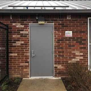 Gray door in a red brick building with a concrete walkway and a small sign nearby