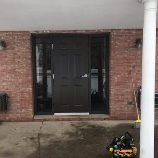 Brick house front entrance with dark door, white column, and a toolbox on the concrete porch.
