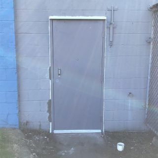 Gray metal door set in a blue cinderblock wall beside a chain-link fence.