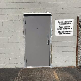 Gray metal door in a cinder block wall beside a warning sign and asphalt lot