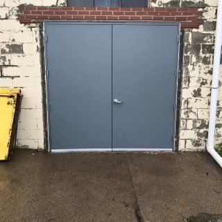 Gray double metal doors set in a brick wall above a wet concrete surface
