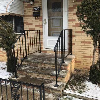 Front entrance with short stone steps, black railings, and a glass door on a brick house with light snow.