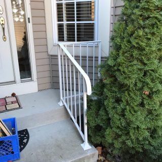 Front porch ramp with white railing beside a window and door, next to a tall evergreen shrub