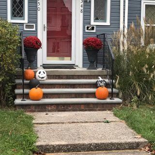Front porch decorated for Halloween with pumpkins, a skull, and red mums by a red door