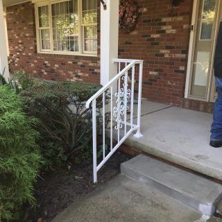 Front porch with steps and a white railing beside a brick house and shrubs