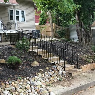 Concrete wheelchair ramp with black railings leading to a house entrance in a landscaped yard