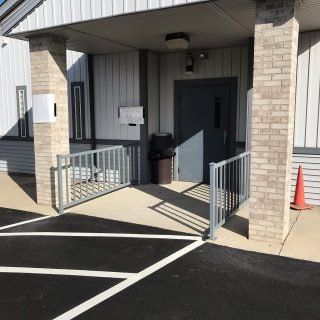 Accessible building entrance with ramp, railings, and a dark door under a covered porch