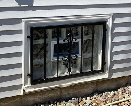 Basement window with black security bars in white vinyl siding above landscaping stones Basement window with black security bars in white vinyl siding above landscaping stones