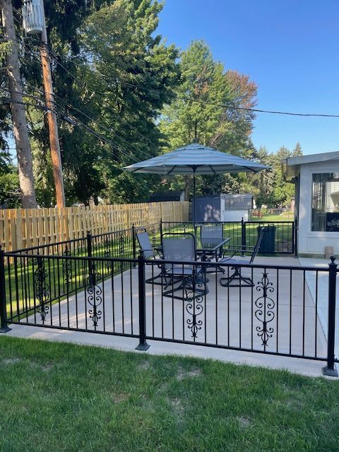 Backyard patio with black railing, umbrella seating, grill, and a small pool or spa beside a house