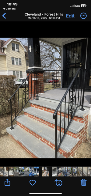 Concrete front steps with orange safety tape, black railings, and a brick house entrance by a sidewalk.