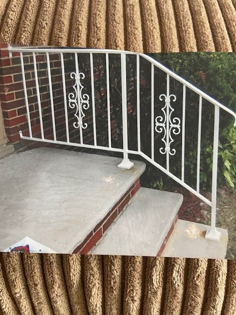 White metal handrail along outdoor concrete steps beside a brick wall and bushes
