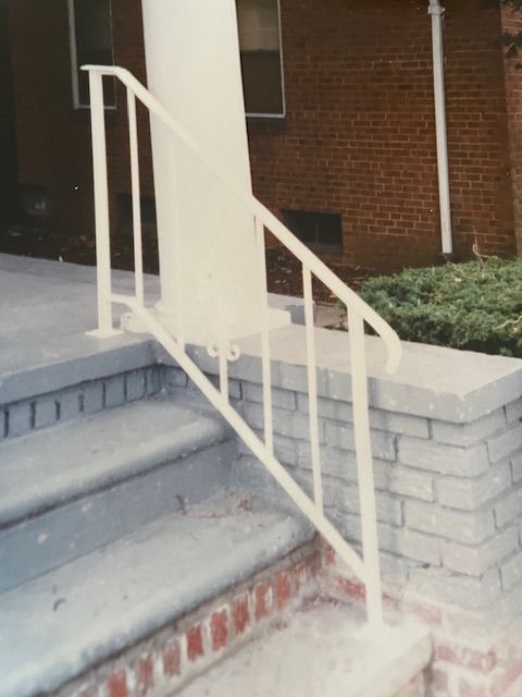 White metal handrail beside concrete steps leading to a brick building entrance
