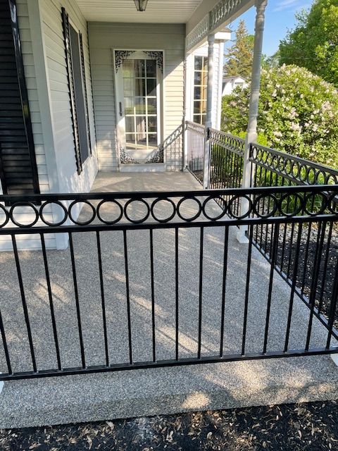 Front porch with black metal railing, concrete steps, and glass-paneled front door in daylight