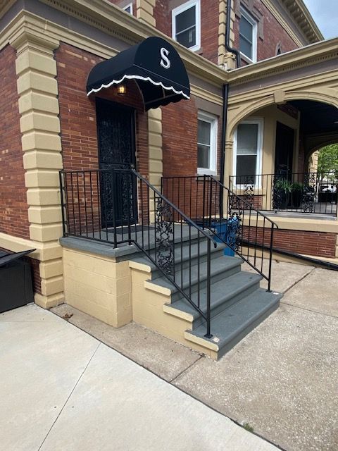 Brick townhouse entrance with black awning, front steps, and metal railings leading to a raised doorway